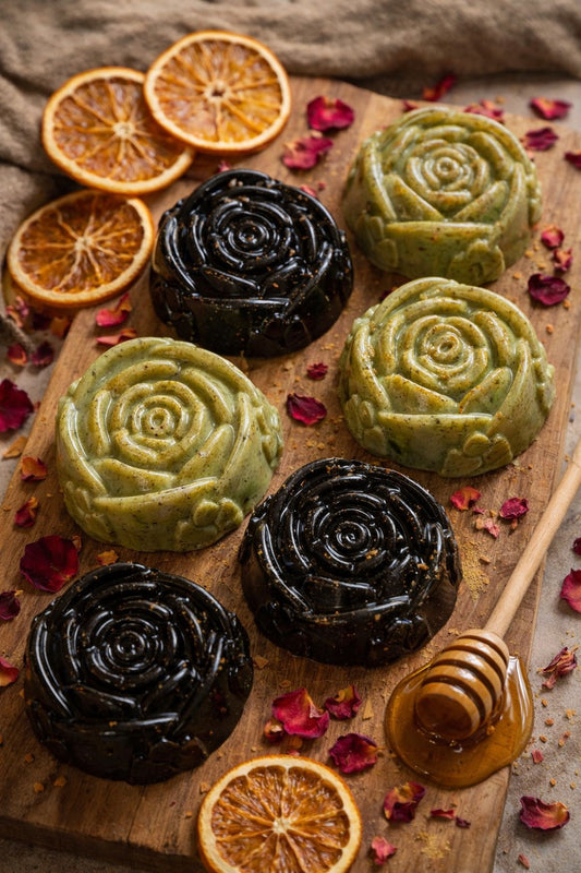 Three green and black pastries on a wooden board with dried oranges and honeycomb.