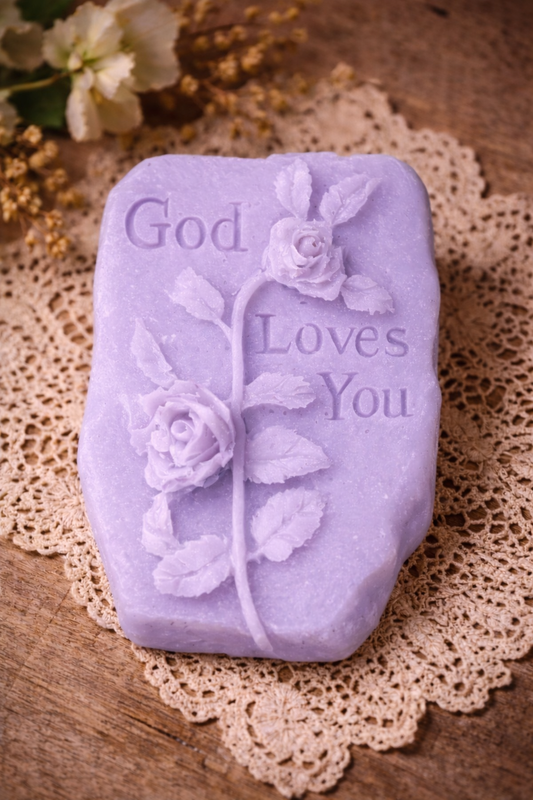 Purple soap bar with 'God Loves You' text and floral designs on a lace doily.
